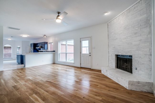Unfurnished living room with a brick fireplace, a ceiling fan, wood finished floors, and baseboards | Image 7