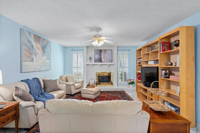 Living room with a textured ceiling, a ceiling fan, a brick fireplace, and tile patterned flooring | Image 6