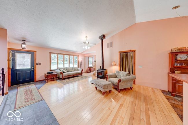living area featuring a wood stove, vaulted ceiling, wood finished floors, a ceiling fan, and a textured ceiling | Image 51