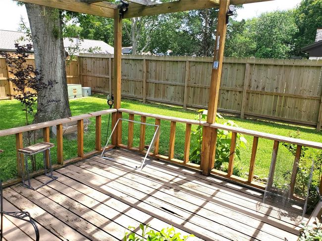 This photo showcases a cozy backyard with a wooden deck and pergola, perfect for relaxing. There's a lush lawn, mature trees, and a privacy fence, offering a serene outdoor space. | Image 14
