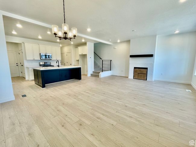 Kitchen with appliances with stainless steel finishes, recessed lighting, light wood finished floors, a tile fireplace, and a chandelier | Image 6
