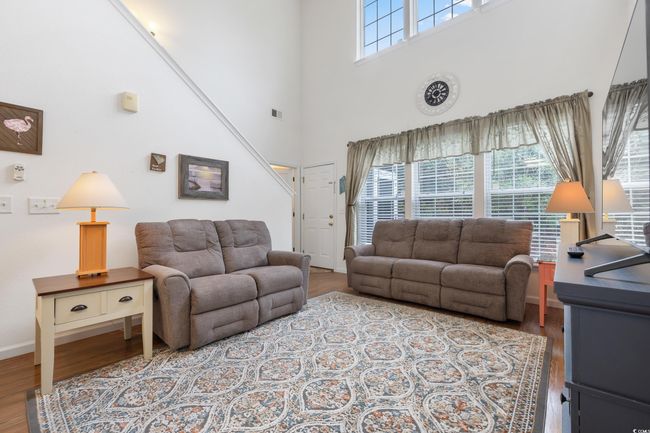 Living area with wood finished floors, a high ceiling, and baseboards | Image 7