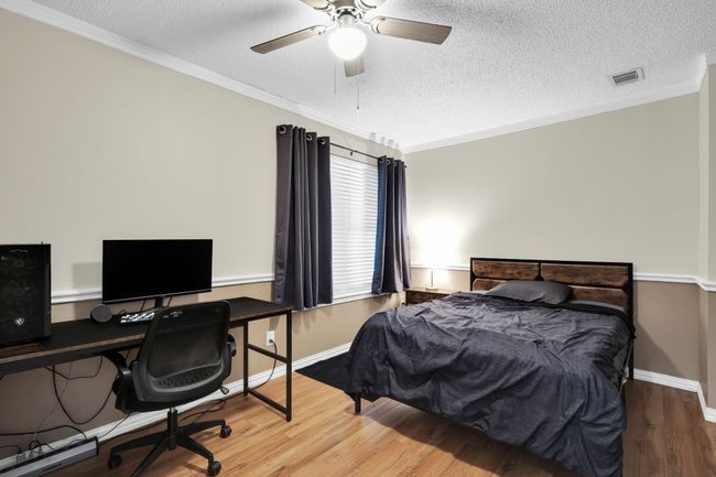 Bedroom featuring wood finished floors, a textured ceiling, crown molding, an office area, and ceiling fan | Image 7
