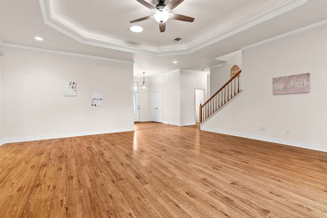 Unfurnished living room with crown molding, ceiling fan, light wood-type flooring, recessed lighting, and a raised ceiling | Image 6