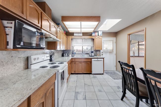 Kitchen featuring a skylight, tasteful granite counters & backsplash, white appliances, and a sink | Image 9