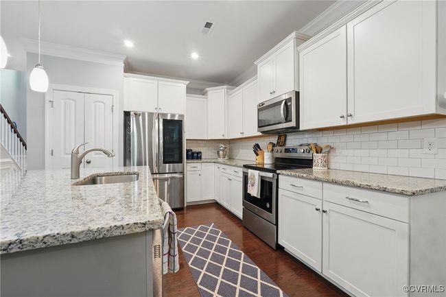 Stylish kitchen with white cabinetry, granite counters, stainless appliances, and tile backsplash. | Image 7