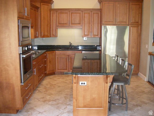Kitchen featuring a center island, a kitchen bar, stainless steel appliances, brown cabinets, and dark stone counters | Image 19