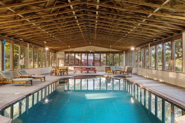 The pool house presents a haven of leisure, highlighted by a generously sized 35, 000-gallon pool. It houses two welcoming guest bedrooms, a complete bathroom, and a well-appointed kitchen area. Bask in the luxury of year-round pool enjoyment, facilitated by rooftop solar panels and an efficient propane pool heater. The screened windows not only invite fresh breezes but also offer picturesque glimpses of the encompassing landscape. | Image 7