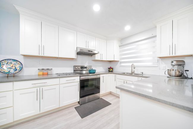 Kitchen featuring a sink, light wood finished floors, under cabinet range hood, white cabinets, and electric range | Image 21