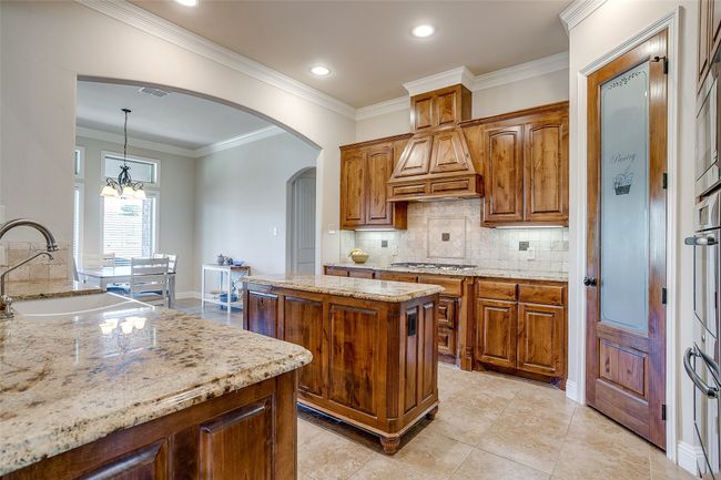 Kitchen with premium range hood, light stone counters, a sink, and ornamental molding | Image 10
