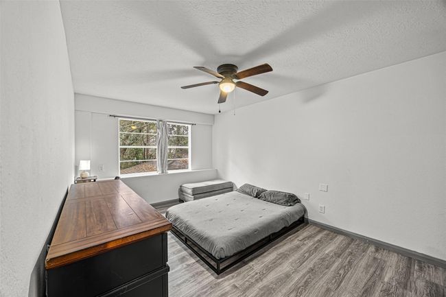 This bedroom features a ceiling fan and natural light from a large window. The neutral walls and wood-style flooring create a calm atmosphere, perfect for relaxation. | Image 20