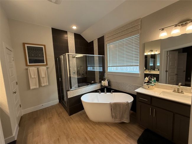 Full bathroom with a stall shower, a freestanding tub, vanity, wood finished floors, and lofted ceiling | Image 14