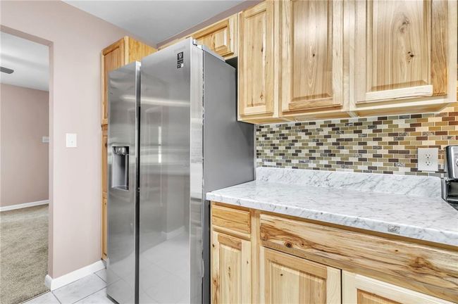 Kitchen featuring stainless steel fridge, light tile patterned flooring, baseboards, decorative backsplash, and light brown cabinets | Image 23