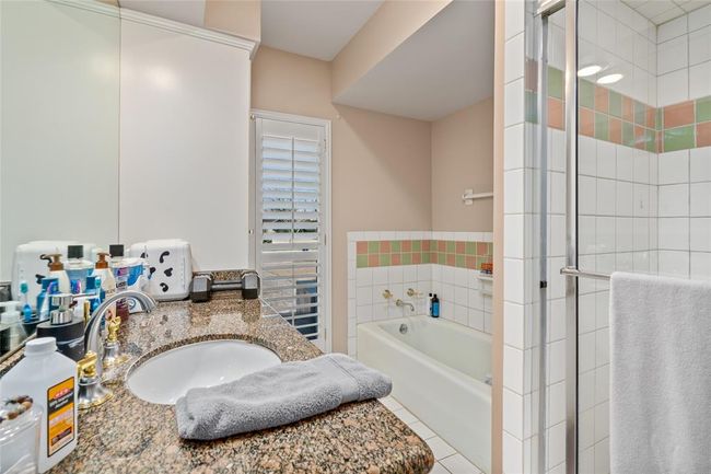 This bathroom features a spacious layout with a combination of a built-in bathtub and a separate glass-enclosed shower. The walls are adorned with neutral tones, complemented by tiled accents. A large vanity area offers ample counter space, and a window with plantation shutters allows for natural light and ventilation. | Image 27