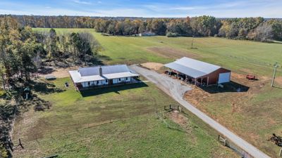 Aerial view of a 40-acre property in Springfield, TN featuring a modern farmhouse with rustic charm, surrounded by lush fields. Also with the property, a large 40x80 shop stands, offering ample space for work or storage. | Image 1