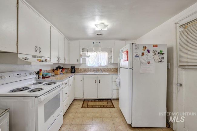Kitchen featuring white appliances, under cabinet range hood, light countertops, and white cabinetry | Image 11