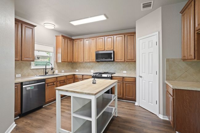 Kitchen featuring appliances with stainless steel finishes, butcher block countertops, a sink, dark wood finished floors, and tasteful backsplash | Image 11