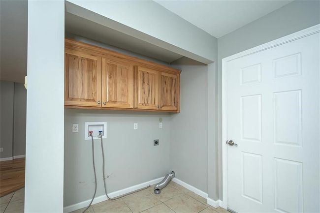 Laundry room featuring electric dryer hookup, washer hookup, cabinet space, light tile patterned floors, and baseboards | Image 19