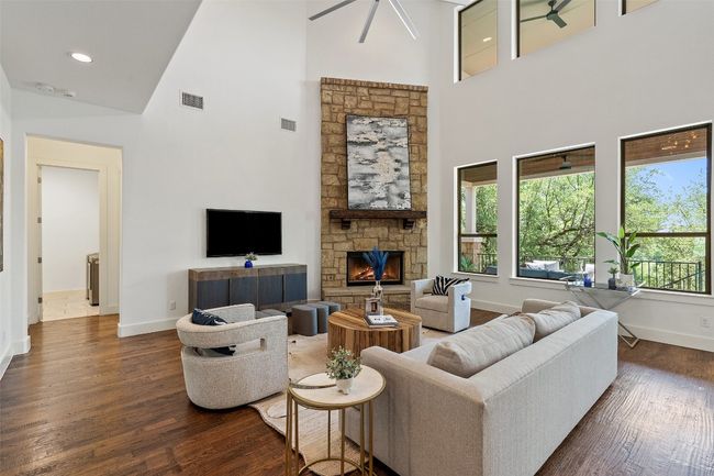 Living room with a towering ceiling, ceiling fan, dark wood-style floors, a fireplace, and recessed lighting | Image 10