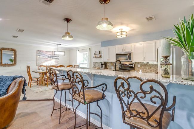 Kitchen with stainless steel microwave, a kitchen breakfast bar, visible vents, and white cabinets | Image 22