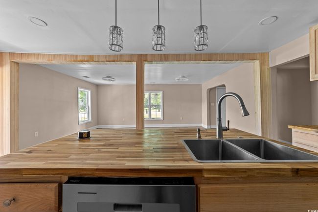Kitchen with wooden counters, open floor plan, dishwasher, wood finished floors, and decorative light fixtures | Image 24