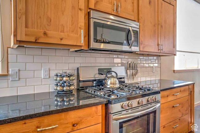 Kitchen featuring appliances with stainless steel finishes, decorative backsplash, brown cabinetry, and dark stone counters | Image 9