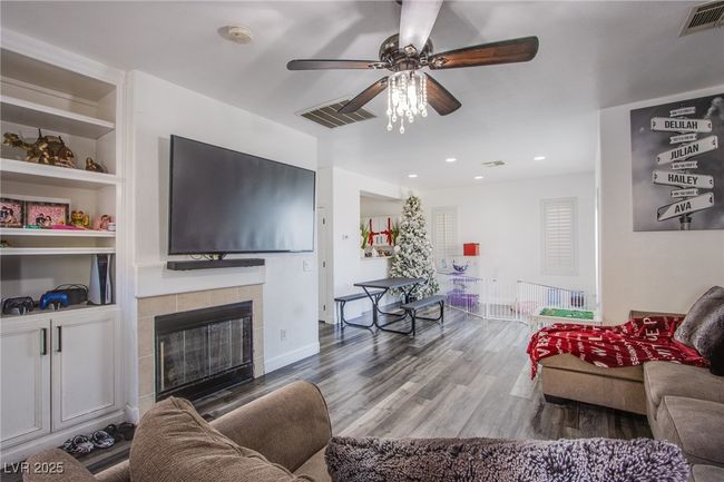 Living room with ceiling fan, wood finished floors, a tile fireplace, built in shelves, and baseboards | Image 9