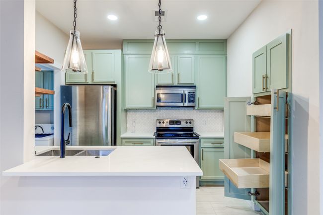 Kitchen featuring appliances with stainless steel finishes, green cabinetry, backsplash, decorative light fixtures, and a peninsula | Image 6
