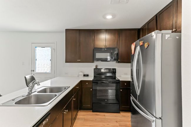 Kitchen featuring black appliances, light wood-style flooring, light countertops, dark brown cabinetry, and a peninsula | Image 16