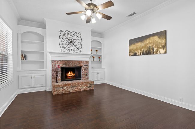 Unfurnished living room with a fireplace, built in features, wood finished floors, ceiling fan, and crown molding | Image 4