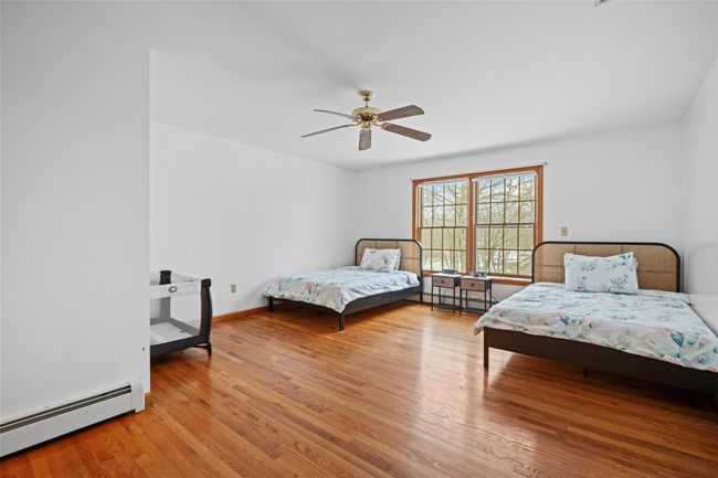 Bedroom with baseboard heating, baseboards, a ceiling fan, and wood finished floors | Image 25