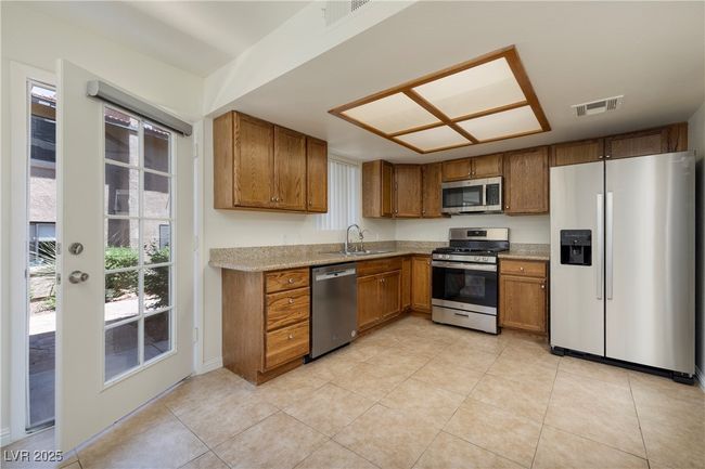 Kitchen with appliances with stainless steel finishes, brown cabinetry, light tile patterned floors, and light countertops | Image 5