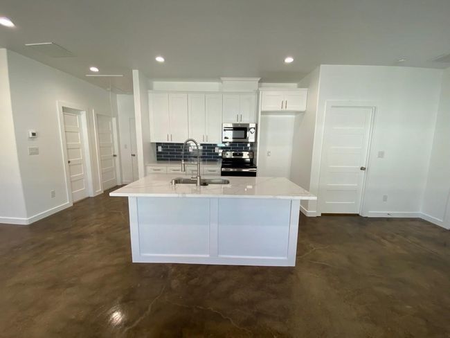 Kitchen with stainless steel appliances, a sink, white cabinets, finished concrete floors, and baseboards | Image 6