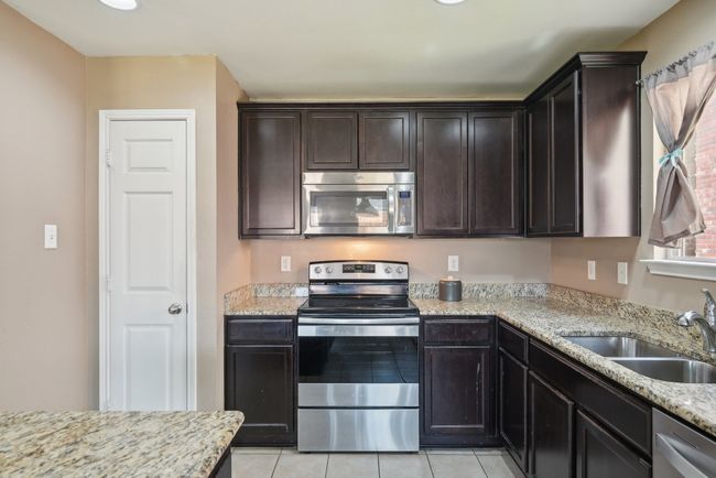 Kitchen featuring light stone counters, a sink, appliances with stainless steel finishes, light tile patterned floors, and dark brown cabinets | Image 11