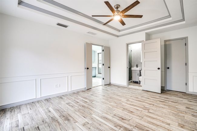 Unfurnished bedroom with a tray ceiling, light wood-type flooring, ensuite bathroom, and a ceiling fan | Image 11