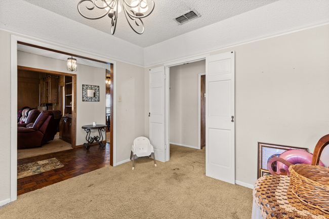 Living area with a textured ceiling, a chandelier, light carpet, baseboards, and visible vents | Image 11