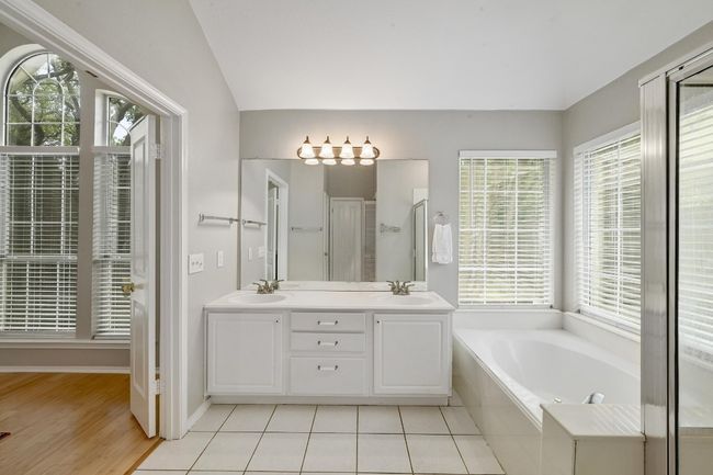 Primary Bathroom featuring a garden tub, double vanity, separate stall shower, lofted ceiling, and tile floors | Image 9