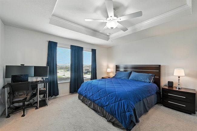 Carpeted bedroom with ornamental molding, a raised ceiling, an office area, and ceiling fan | Image 24