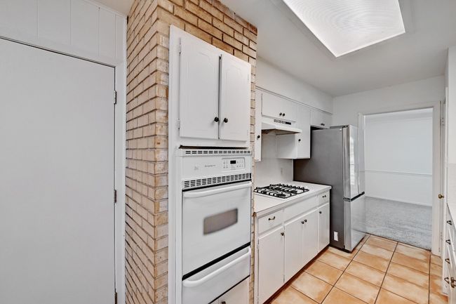 Kitchen featuring light tile patterned floors, white appliances, white cabinetry, a warming drawer, and under cabinet range hood | Image 13