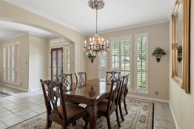 Elegant dining room with a sparkling chandelier, plantation shutters, and views of the front yard. | Image 6