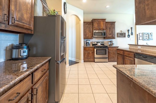 Kitchen featuring appliances with stainless steel finishes, light tile patterned floors, dark stone countertops, decorative backsplash, and recessed lighting | Image 11