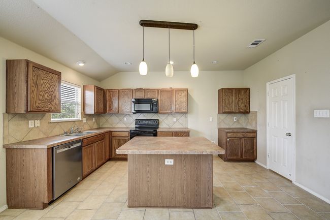 Kitchen featuring decorative backsplash, brown cabinetry, decorative light fixtures, black appliances, and light countertops | Image 11