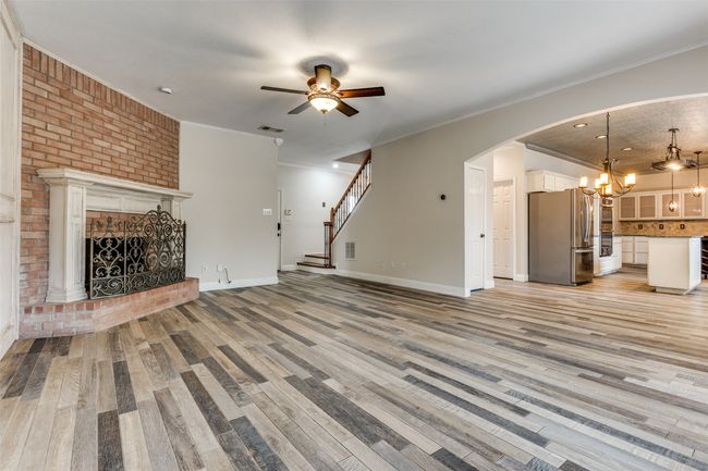 Unfurnished living room with visible vents, a brick fireplace, crown molding, light wood-style flooring, and arched walkways | Image 6