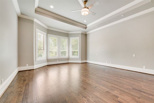 Empty room featuring a tray ceiling, wood finished floors, a ceiling fan, crown molding, and baseboards | Image 21