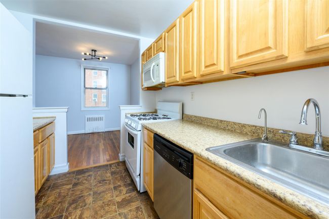 Kitchen featuring sink, white appliances, radiator heating unit, light stone counters, and light brown cabinetry | Image 8