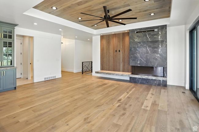 Unfurnished living room with a raised ceiling, wood ceiling, recessed lighting, light wood-style flooring, and a high end fireplace | Image 16