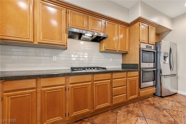 Kitchen with appliances with stainless steel finishes, under cabinet range hood, decorative backsplash, dark stone countertops, and brown cabinets | Image 7