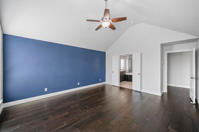 Unfurnished bedroom with ensuite bath, wood finished floors, baseboards, and high vaulted ceiling | Image 24