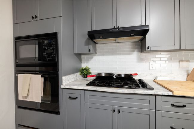 Kitchen with gray cabinets, under cabinet range hood, decorative backsplash, and black appliances | Image 16