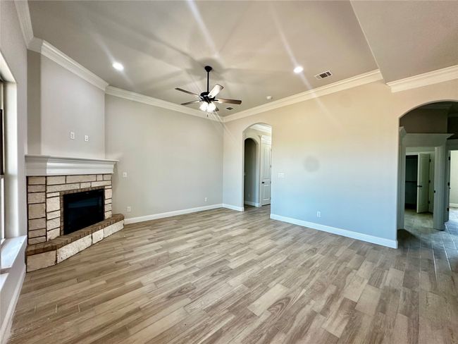 Unfurnished living room featuring arched walkways, a ceiling fan, wood finished floors, recessed lighting, and crown molding | Image 6